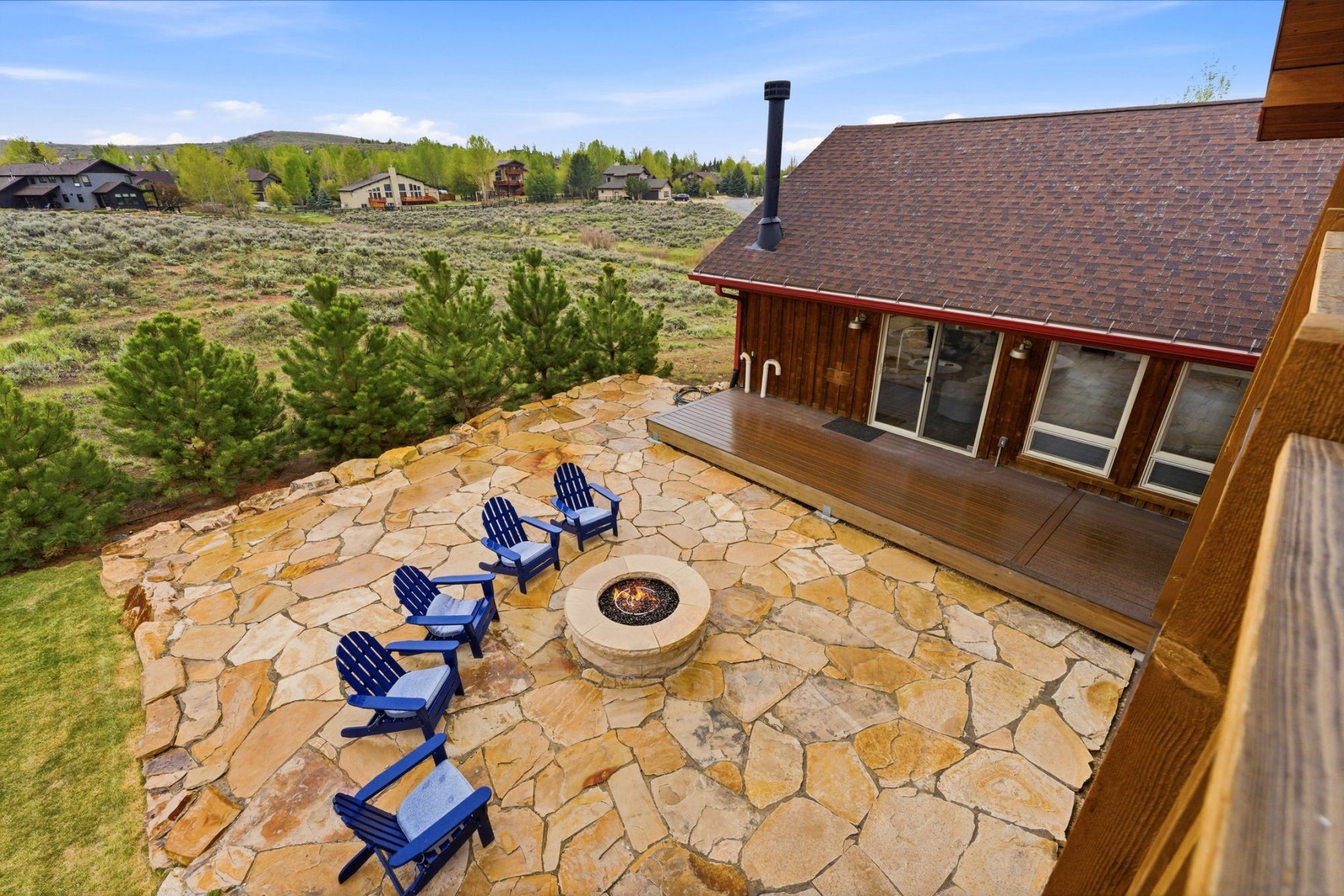 Expansive flagstone patio featuring a built-in fire pit, surrounded by natural landscaping and mature trees