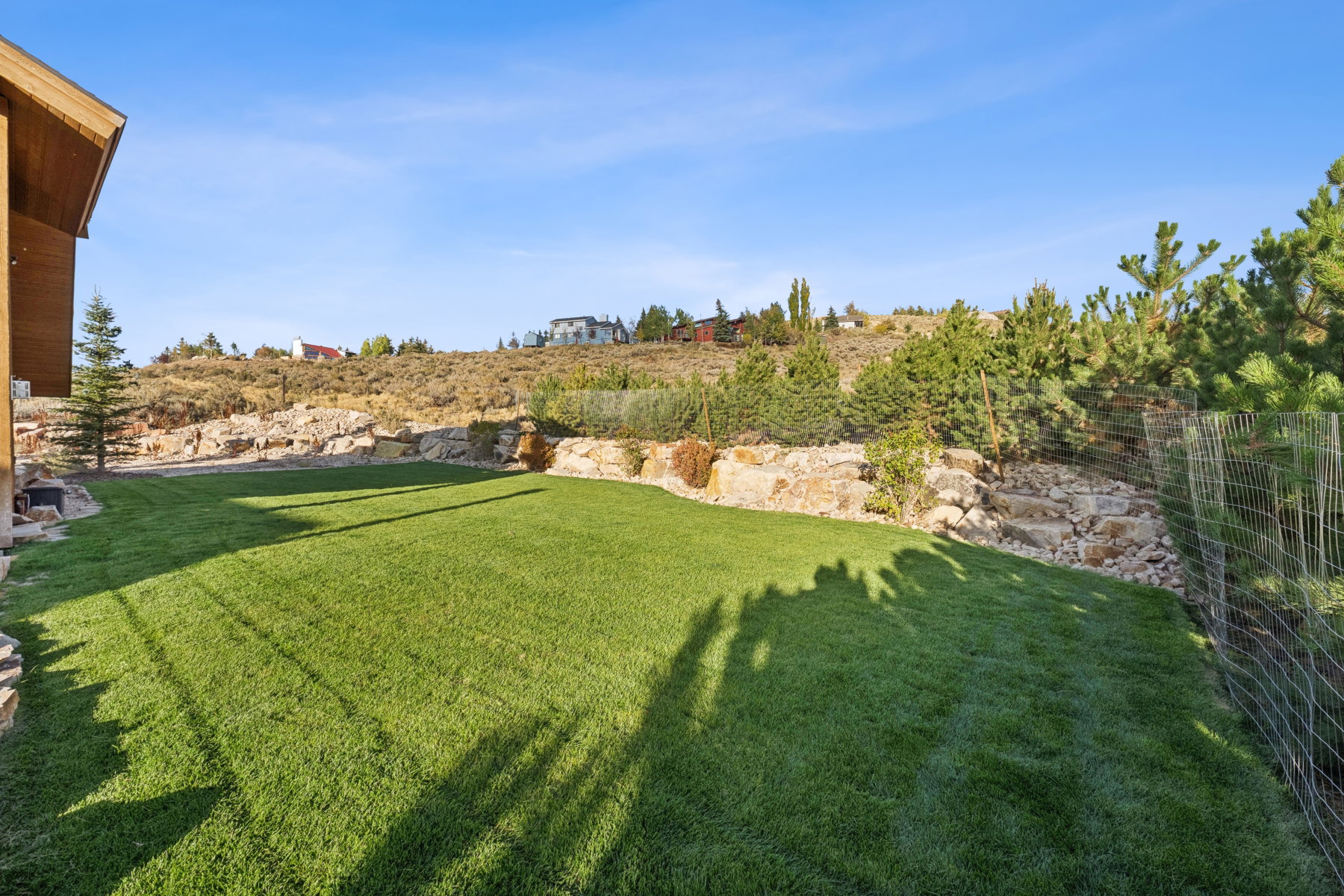 Expansive grassy lawn bordered by natural rock retaining walls and mature evergreen landscaping