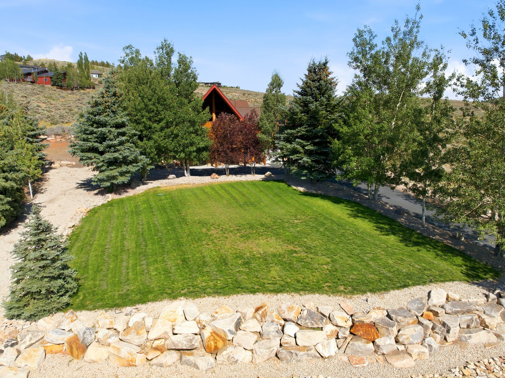 Level lawn area surrounded by a natural stone retaining wall and mature evergreen and deciduous trees