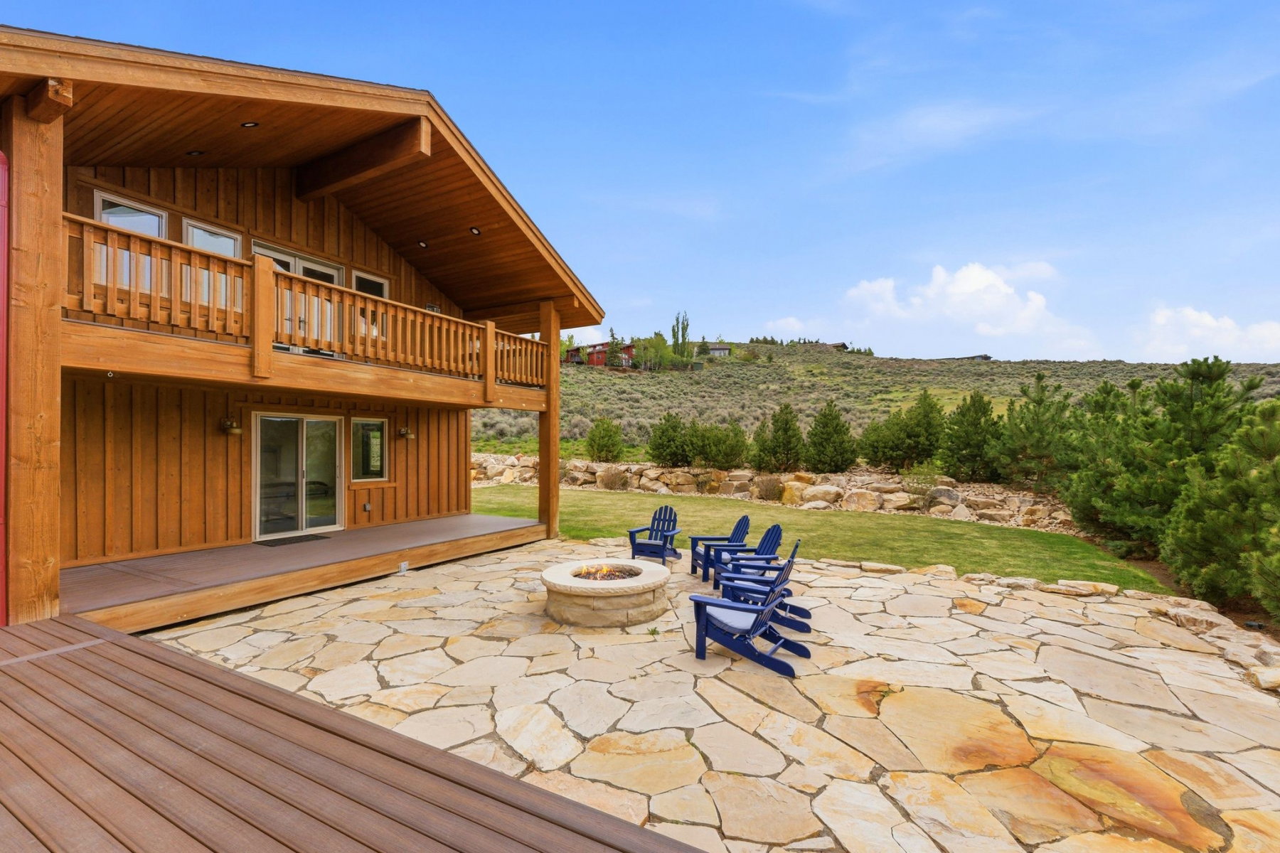 Expansive outdoor living area featuring a flagstone patio, a built-in fire pit, and a spacious wood-finish deck
