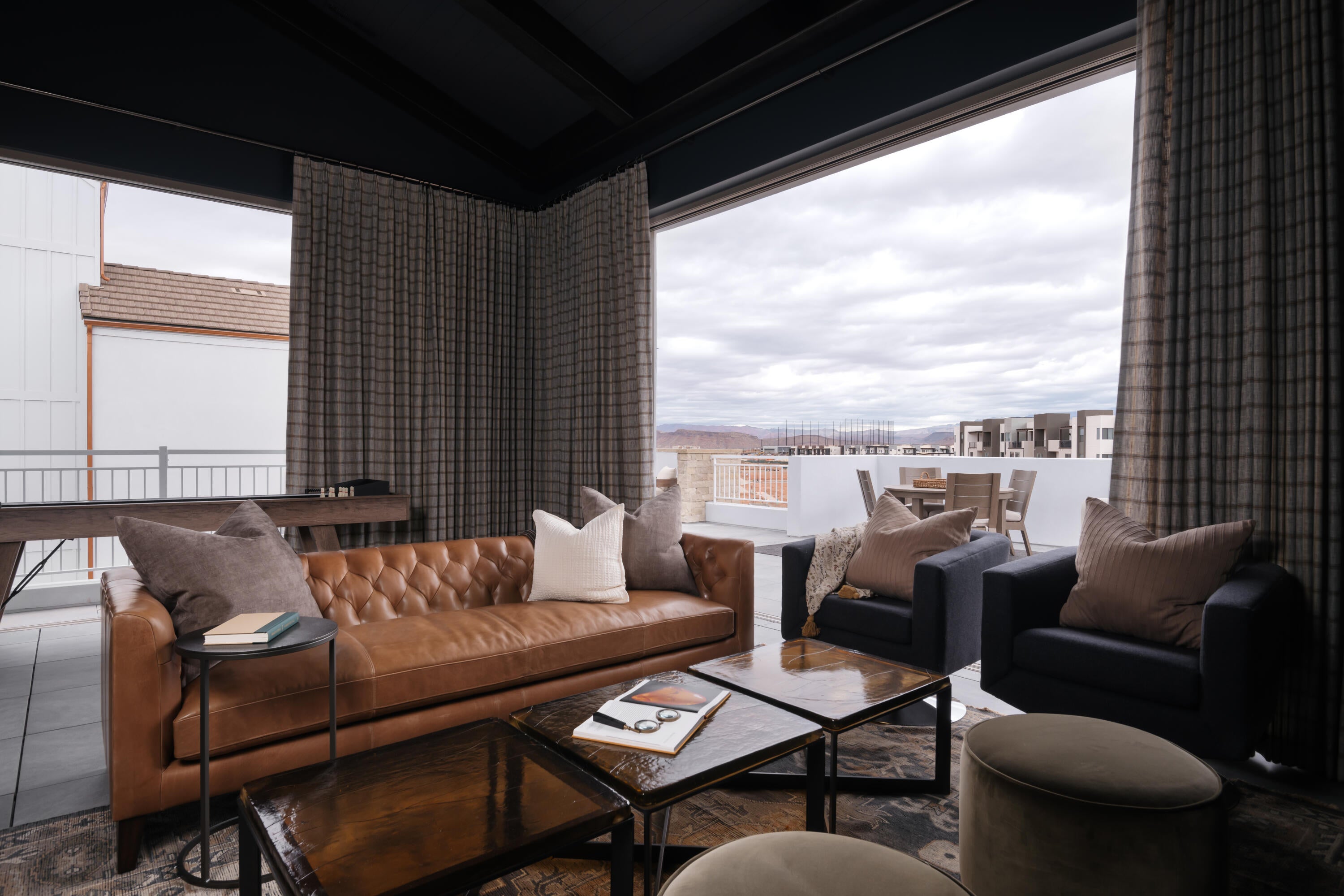 Expansive indoor-outdoor living area featuring large sliding glass doors, a dark coffered ceiling, and patterned floor-to-ceiling drapery