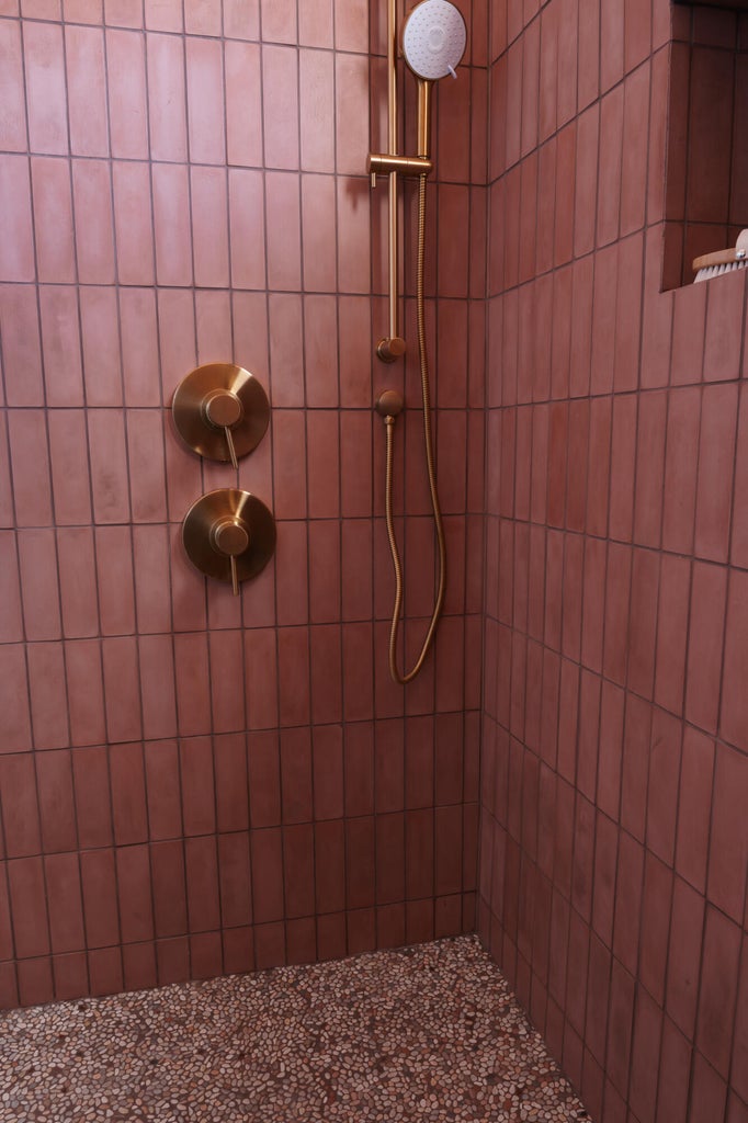 Shower with vertical subway tile in a terracotta hue, featuring brass fixtures including a rain shower head and handheld sprayer