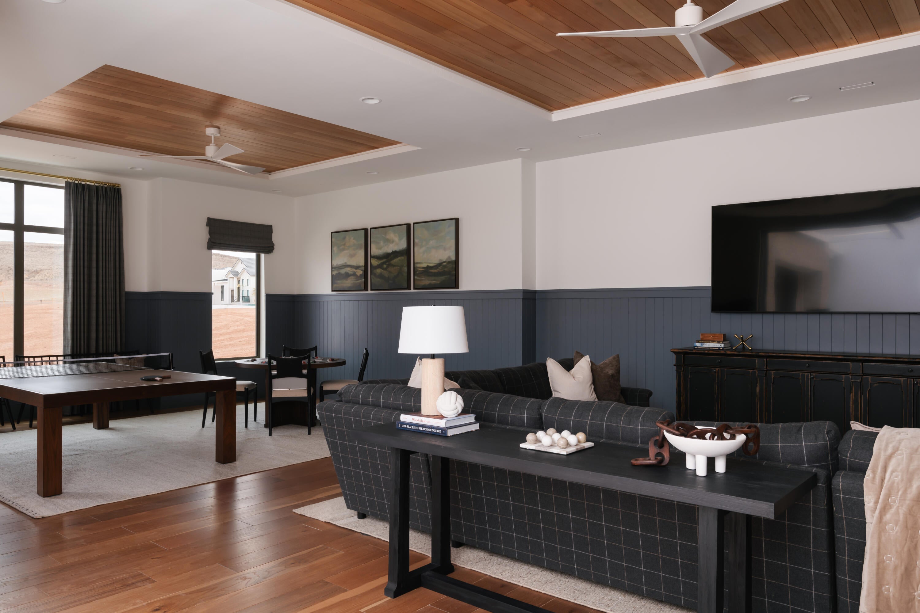 Expansive room featuring wood-finish flooring, a wood-paneled ceiling treatment, large windows with dark drapery, and beadboard wainscoting