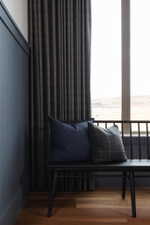 Vertical paneling with a rich blue finish, complemented by full-length dark drapery and wood-finish flooring