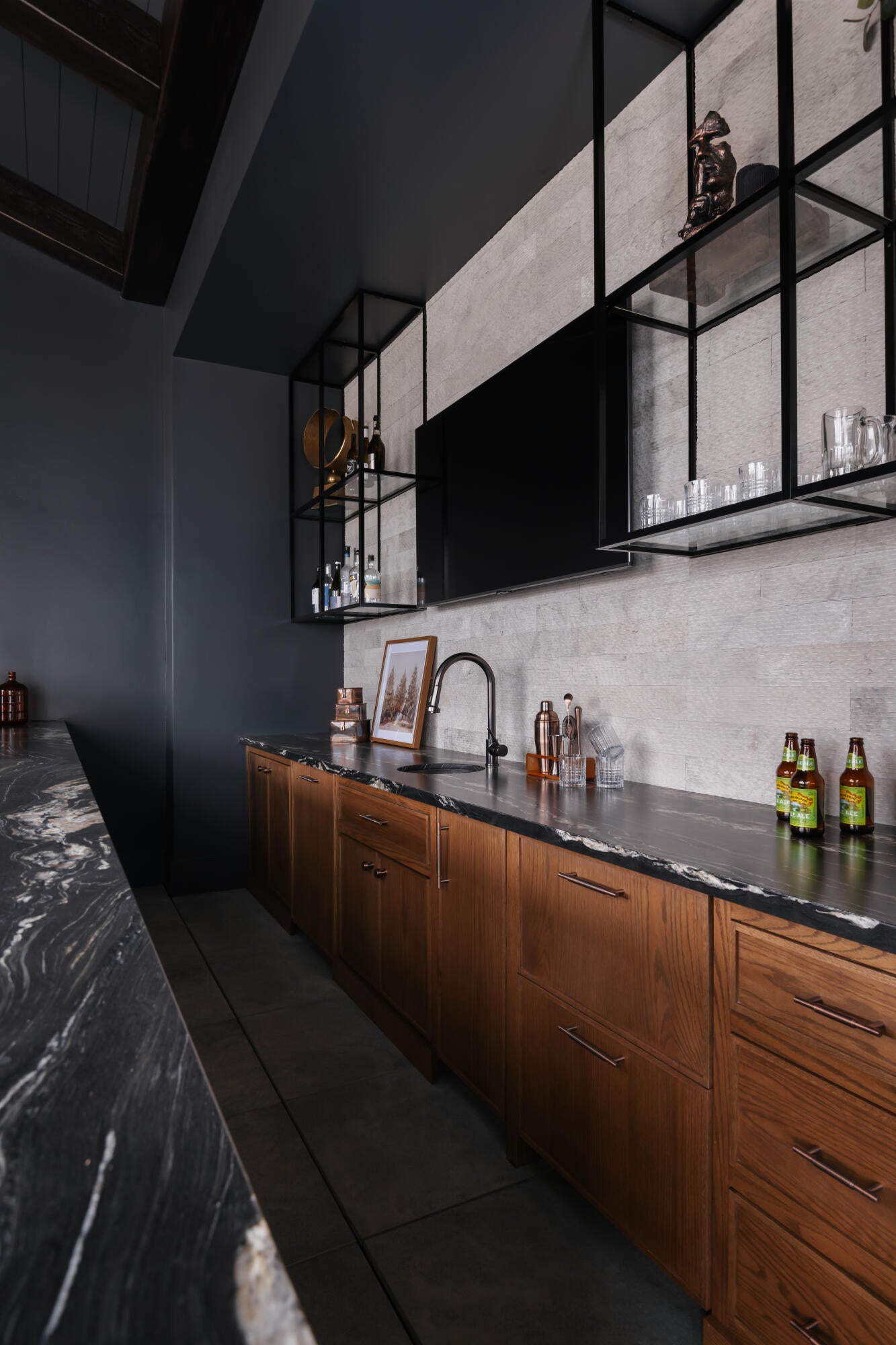 Wet bar featuring an integrated sink with a matte black faucet, wood-finish cabinetry, and dark stone countertops