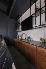 Wet bar featuring an integrated sink with a matte black faucet, wood-finish cabinetry, and dark stone countertops