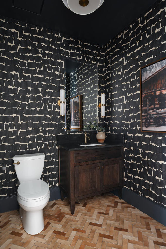 Powder room featuring a dark wood vanity with a stone countertop, a rectangular mirror flanked by brass sconces, and herringbone wood-finish flooring