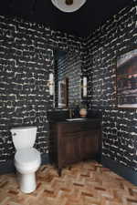 Powder room featuring a dark wood vanity with a stone countertop, a rectangular mirror flanked by brass sconces, and herringbone wood-finish flooring