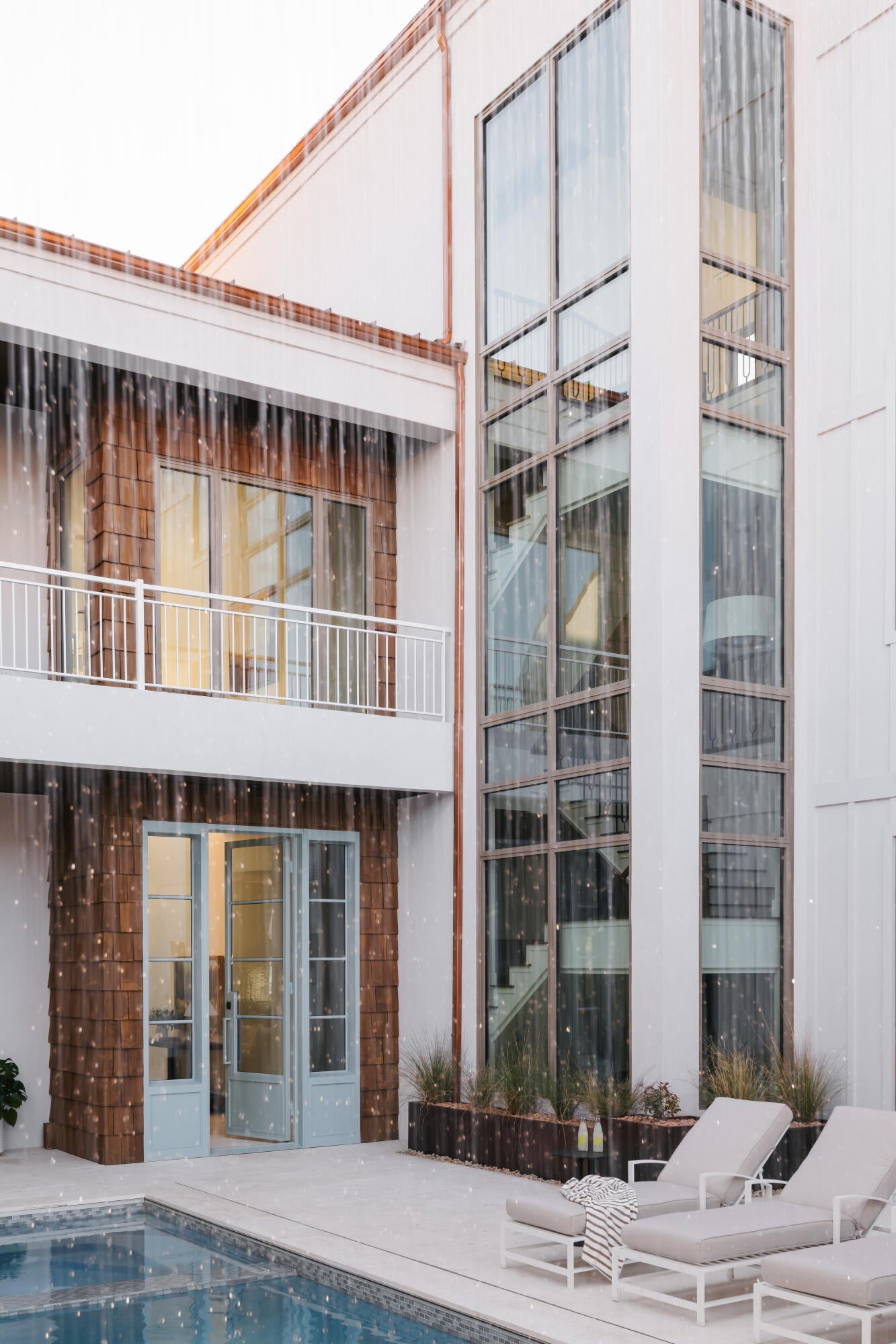 Contemporary exterior featuring a multi-story glass facade, a private balcony with white railing, wood shingle accents, and a swimming pool with surrounding patio