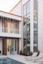 Contemporary exterior featuring a multi-story glass facade, a private balcony with white railing, wood shingle accents, and a swimming pool with surrounding patio