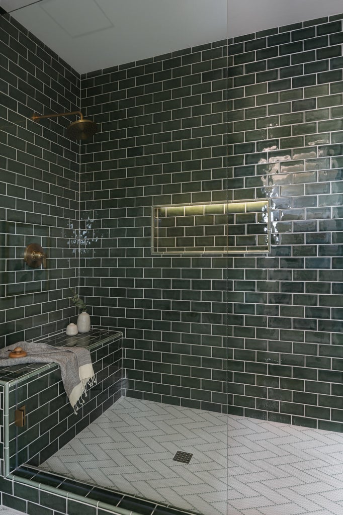 Spacious walk-in shower featuring dark green subway tile walls, a built-in bench, a recessed niche with integrated lighting, and white herringbone tile flooring