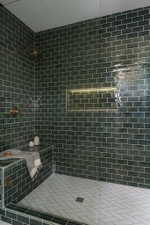 Spacious walk-in shower featuring dark green subway tile walls, a built-in bench, a recessed niche with integrated lighting, and white herringbone tile flooring