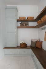 Built-in cabinetry with light blue-gray finish, wood-finish countertops, open wood-finish shelving, integrated storage drawers, and light-colored tile flooring