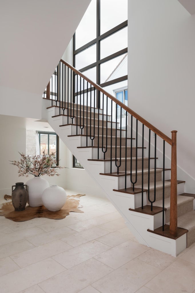 Grand staircase featuring wood-finish handrails, black metal balusters, and carpeted treads