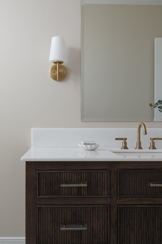 Bathroom vanity featuring a dark wood finish with reeded detailing, white countertop, and gold-toned faucet