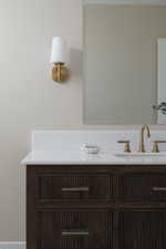 Bathroom vanity featuring a dark wood finish with reeded detailing, white countertop, and gold-toned faucet
