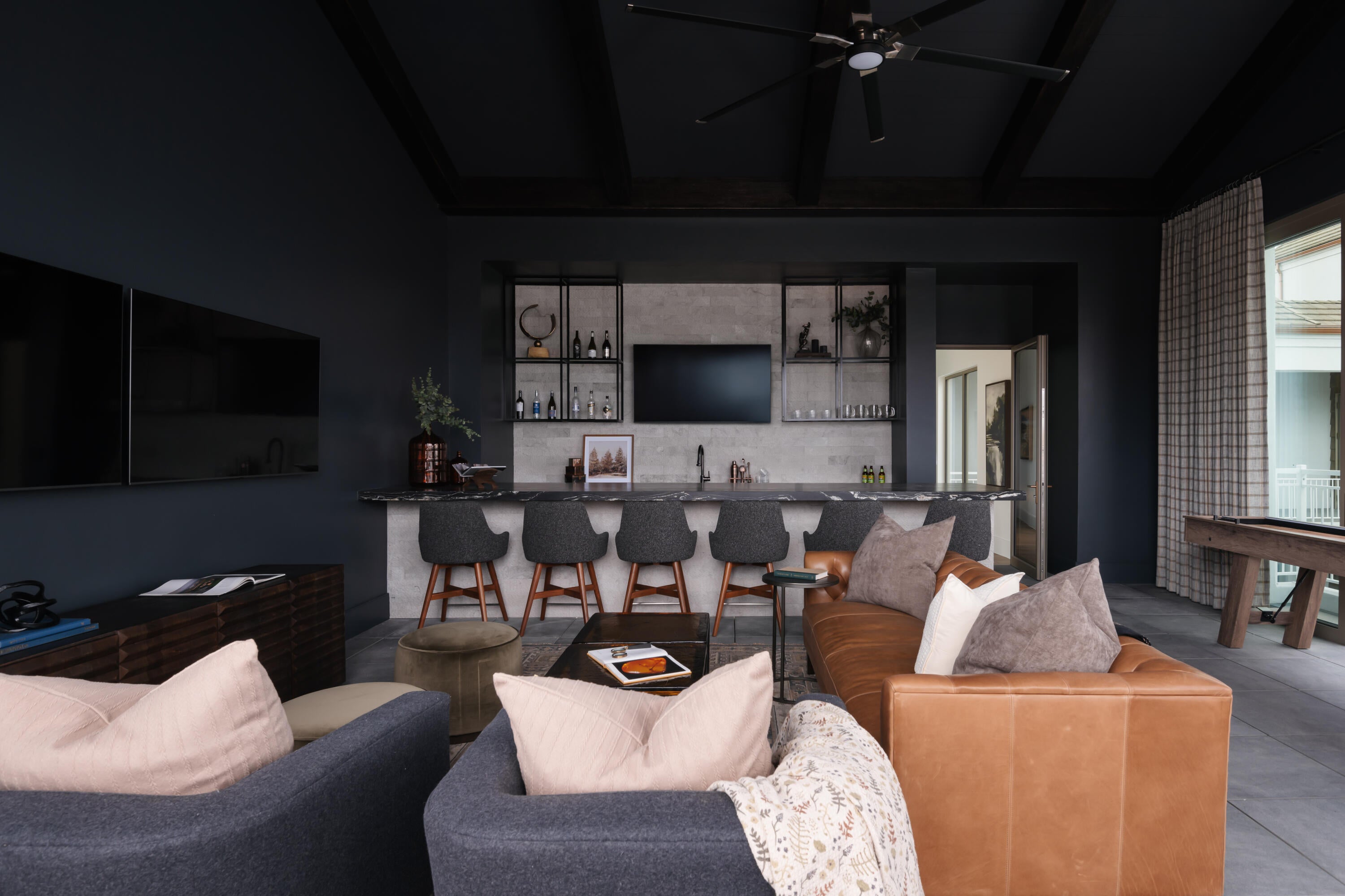 Entertainment room featuring a wet bar with stone countertops and open shelving, a coffered ceiling with a ceiling fan, and large format tile flooring