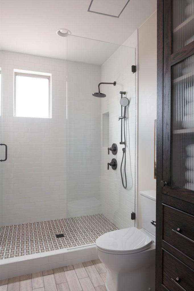 Frameless glass shower enclosure featuring white subway tile walls and a basketweave tile floor