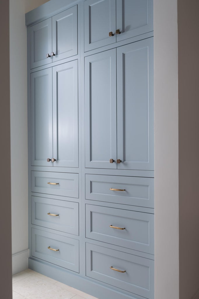 Full-height built-in cabinetry featuring a soft blue finish, recessed panel doors, and brass hardware