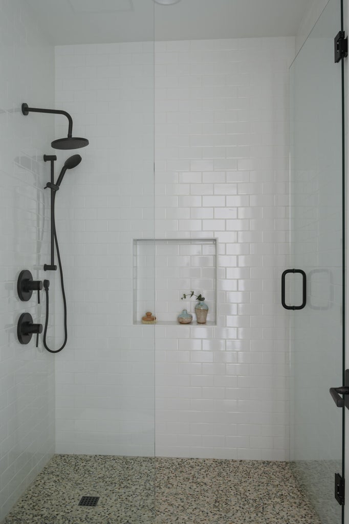 Walk-in shower featuring white subway tile, a recessed niche, black fixtures, and a glass enclosure with black framing