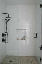 Walk-in shower featuring white subway tile, a recessed niche, black fixtures, and a glass enclosure with black framing