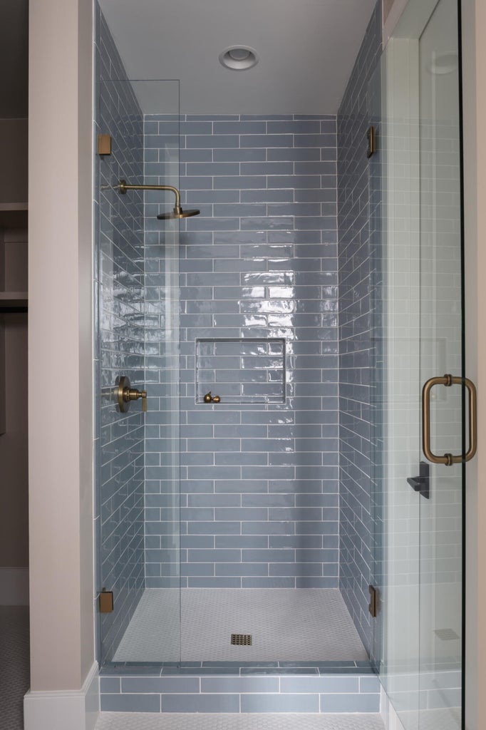Walk-in shower with full glass enclosure, blue subway tile surround, recessed niche, and hexagonal mosaic tile flooring, accented by brass fixtures