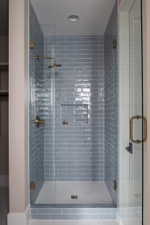 Walk-in shower with full glass enclosure, blue subway tile surround, recessed niche, and hexagonal mosaic tile flooring, accented by brass fixtures