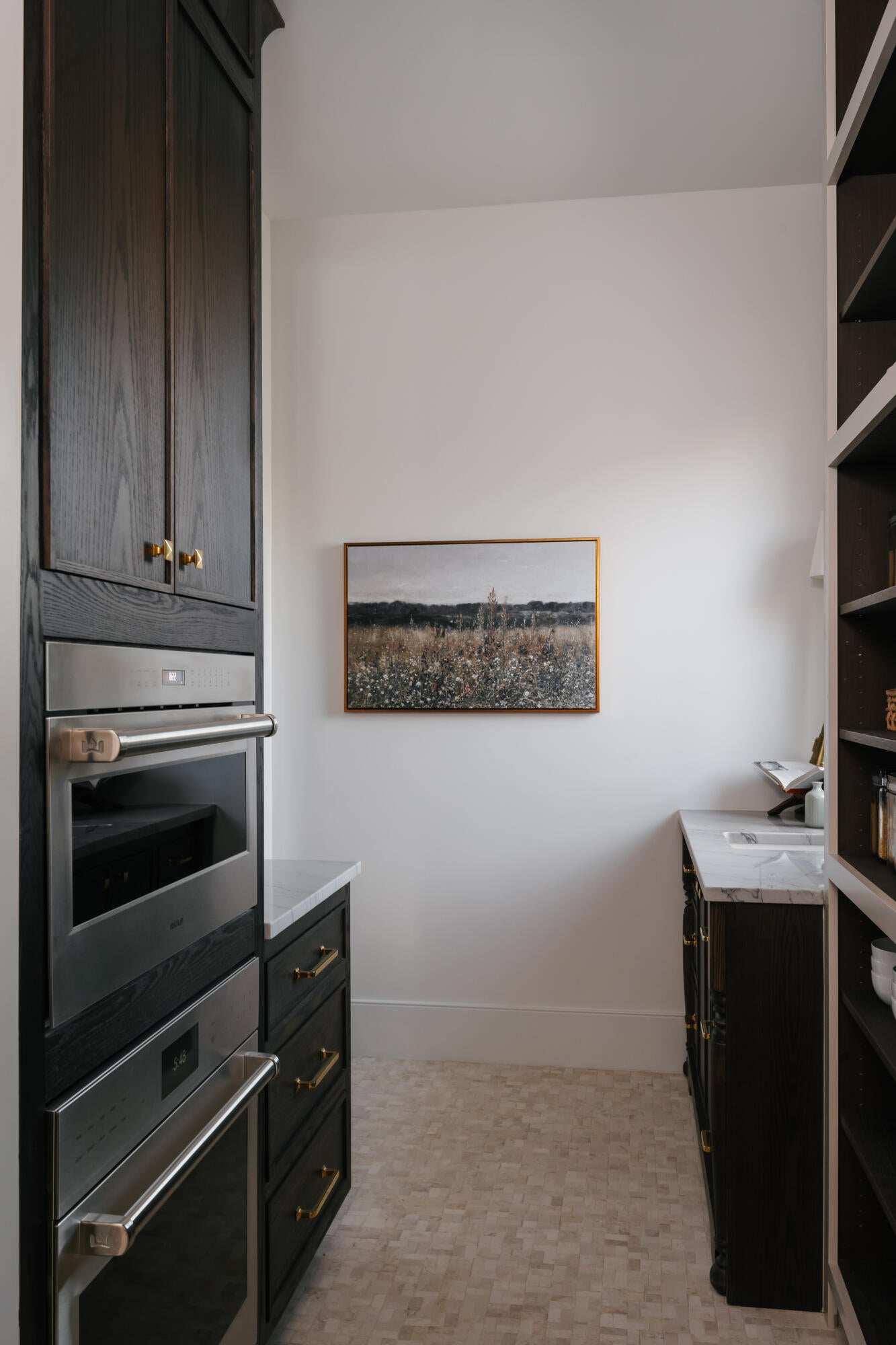 Built-in stainless steel appliances, dark wood cabinetry with brass hardware, marble countertops, and light-toned mosaic tile flooring