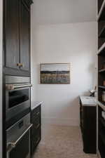Built-in stainless steel appliances, dark wood cabinetry with brass hardware, marble countertops, and light-toned mosaic tile flooring