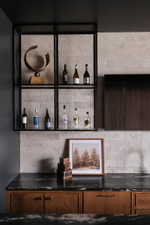 Built-in dry bar featuring black granite countertops, wood cabinetry, a textured backsplash, and open metal shelving