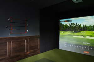 Dedicated golf simulator room featuring a large projection screen, dark wall finishes, and a green turf floor