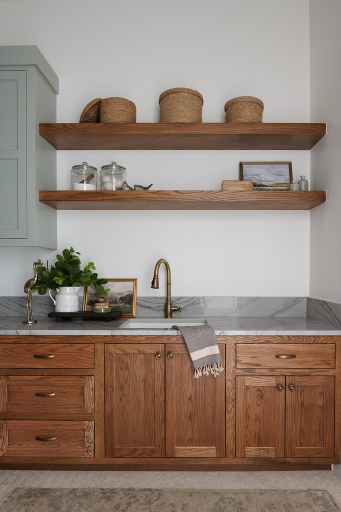 Warm wood-finish cabinetry with brass hardware, a white undermount sink, and a brass gooseneck faucet
