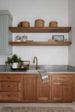 Warm wood-finish cabinetry with brass hardware, a white undermount sink, and a brass gooseneck faucet
