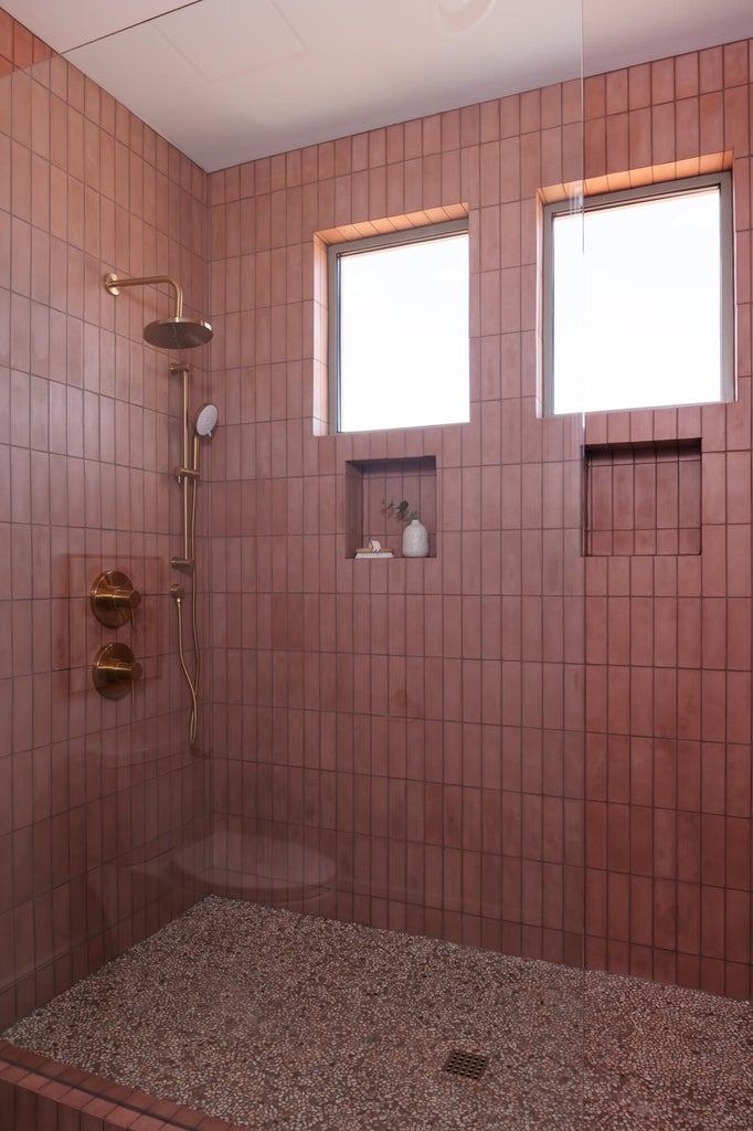 Shower enclosure featuring vertical-stacked tile walls, an exposed pebble floor, and dual recessed niches