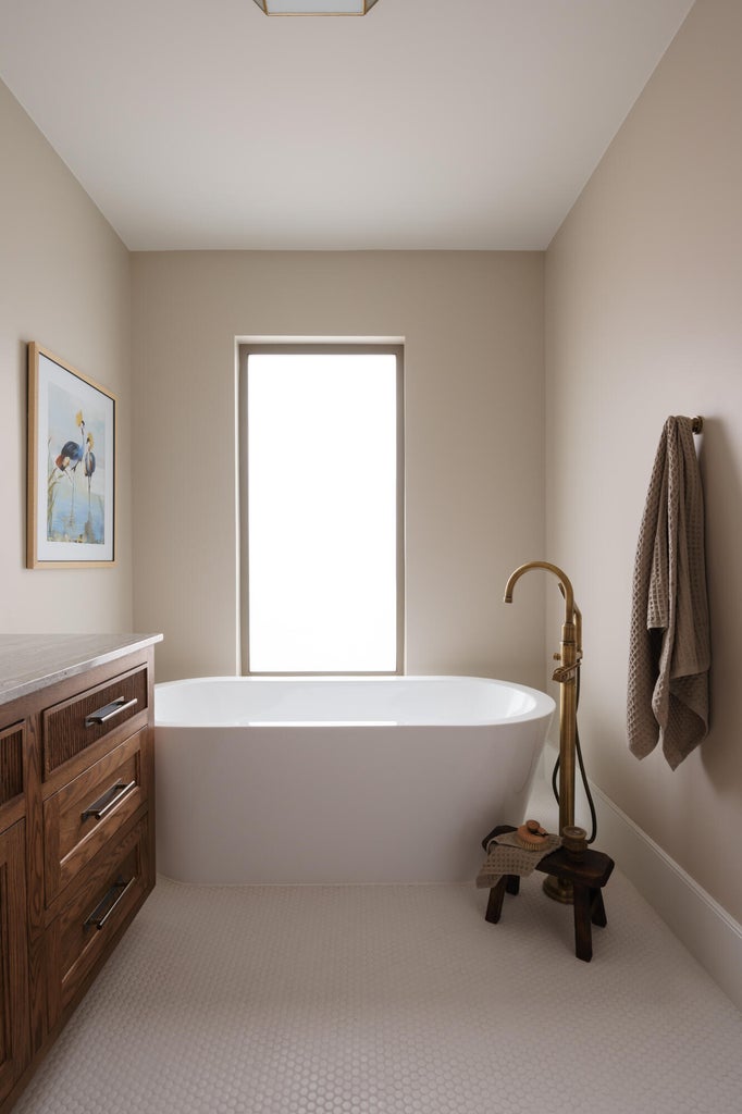Freestanding soaking tub with floor-mounted brass faucet, set against a window