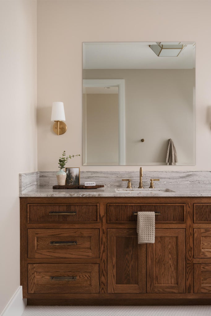 Wood-finish vanity with fluted detailing and dark hardware, topped with a light-toned stone countertop featuring an undermount sink