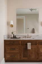Wood-finish vanity with fluted detailing and dark hardware, topped with a light-toned stone countertop featuring an undermount sink