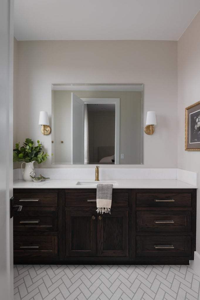 Bathroom vanity featuring a dark wood-finish cabinet with silver hardware, a white countertop, and an integrated rectangular sink with a gold-tone faucet
