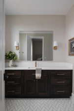 Bathroom vanity featuring a dark wood-finish cabinet with silver hardware, a white countertop, and an integrated rectangular sink with a gold-tone faucet