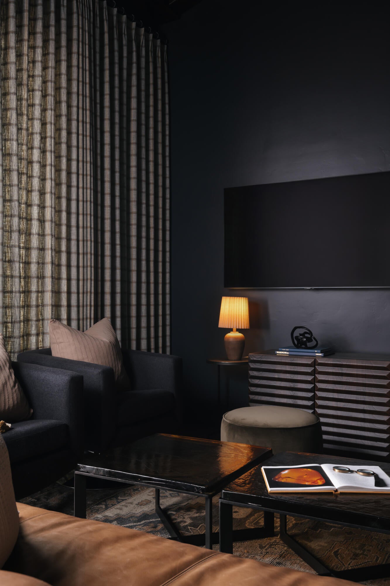 Dark-toned room featuring a large mounted display, full-height drapery, and dark walls