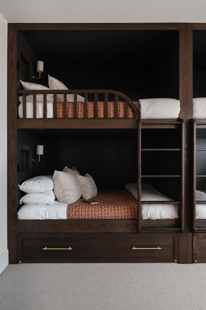 Built-in bunk beds with dark wood-finish framing, integrated ladders, and brass pull hardware on lower storage drawers