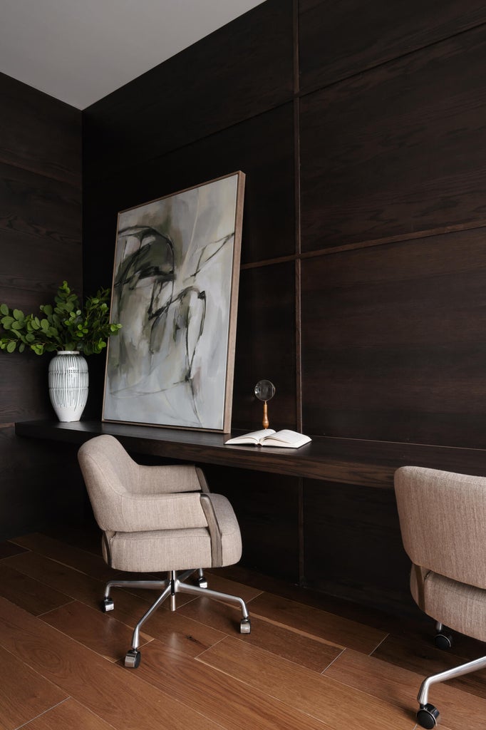Dedicated workspace featuring rich wood-finish wall paneling, a full-width built-in desk, and warm wood-finish flooring