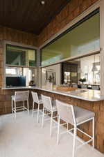 Outdoor bar area featuring a wood-shingle exterior, light-toned flooring, a light-colored countertop, and a dark wood-paneled ceiling