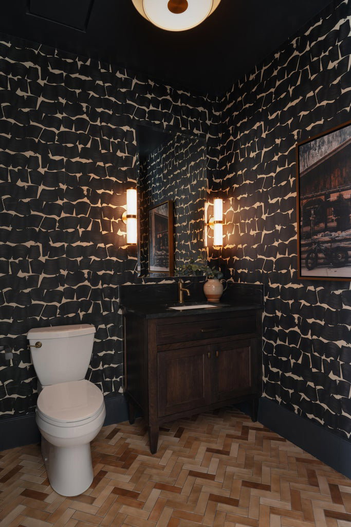 Powder room featuring contemporary patterned wallpaper, dark wood vanity with a black countertop, and recessed mirror with dual sconce lighting