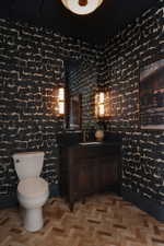 Powder room featuring contemporary patterned wallpaper, dark wood vanity with a black countertop, and recessed mirror with dual sconce lighting