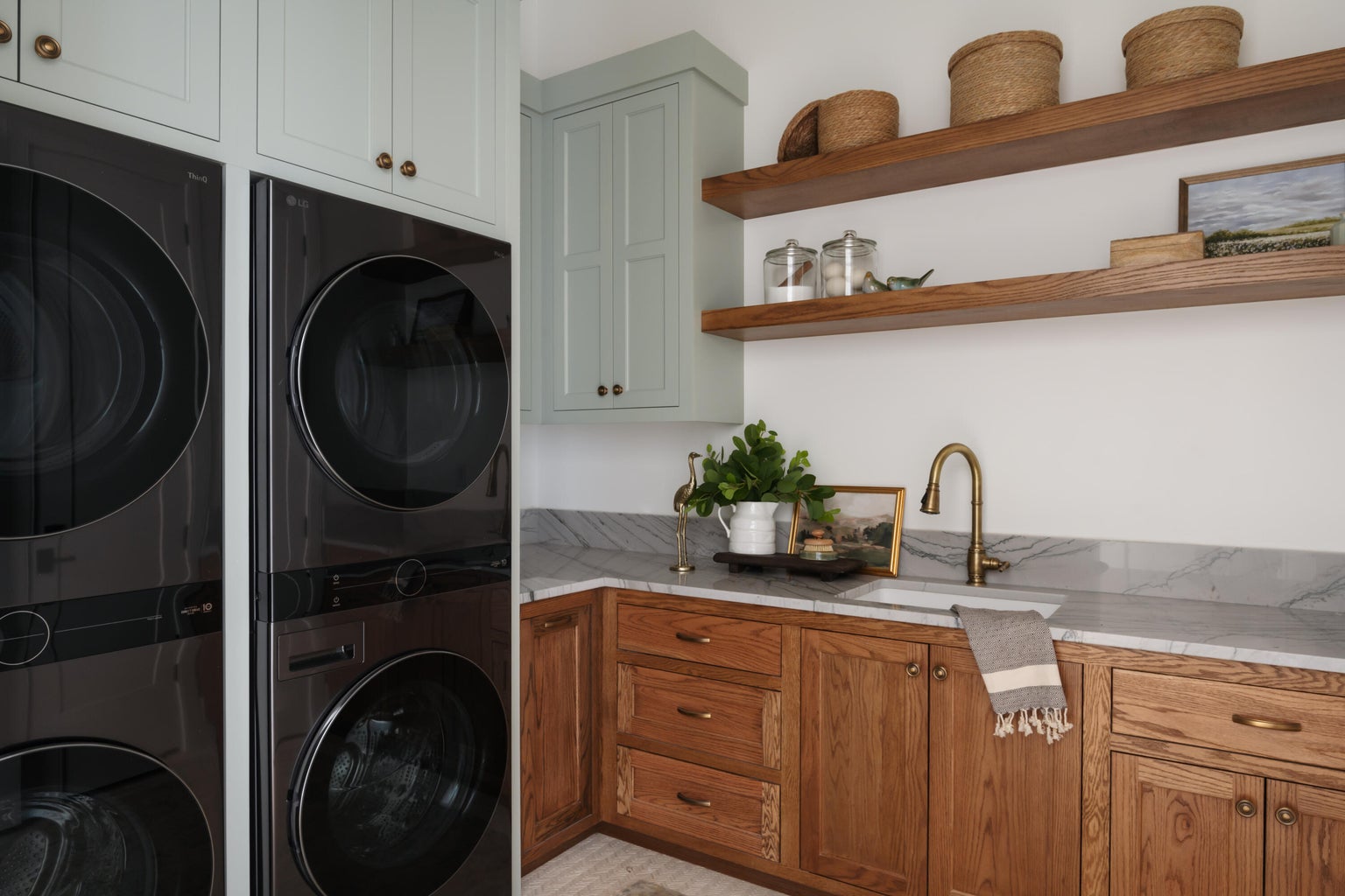 Laundry area featuring stacked washer and dryer units, light green upper cabinetry, and natural wood-finish lower cabinetry