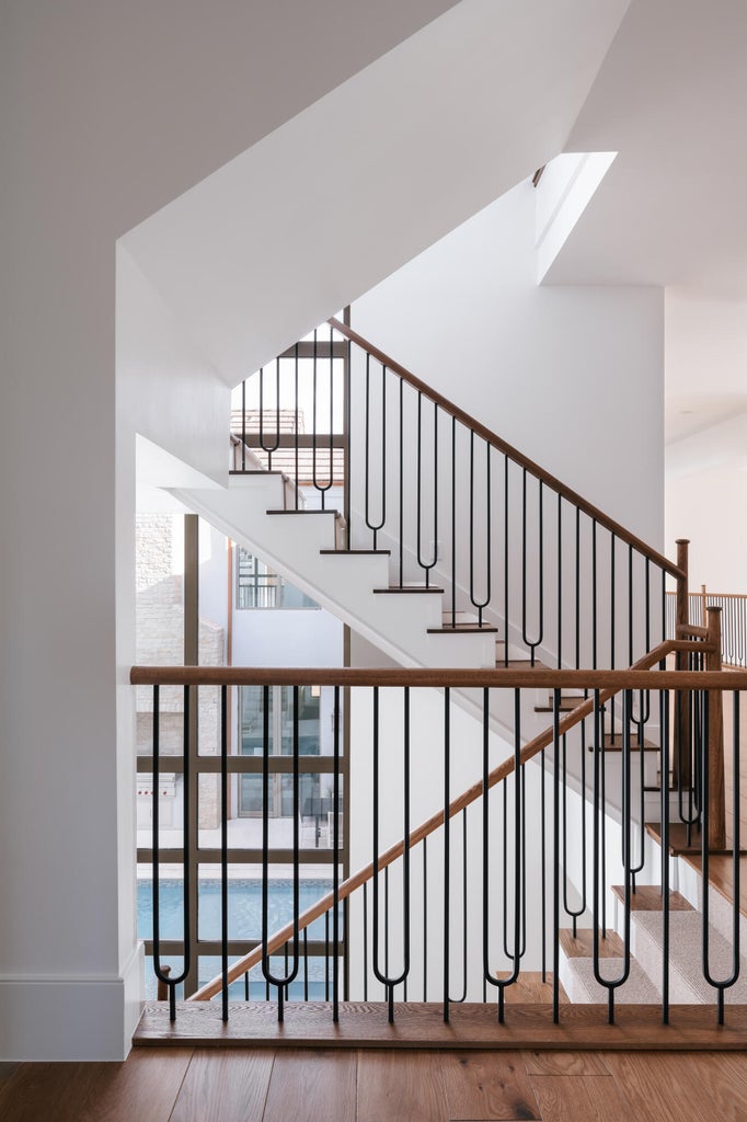 Multilevel staircase featuring black metal balusters with unique u-shaped elements and light wood handrails