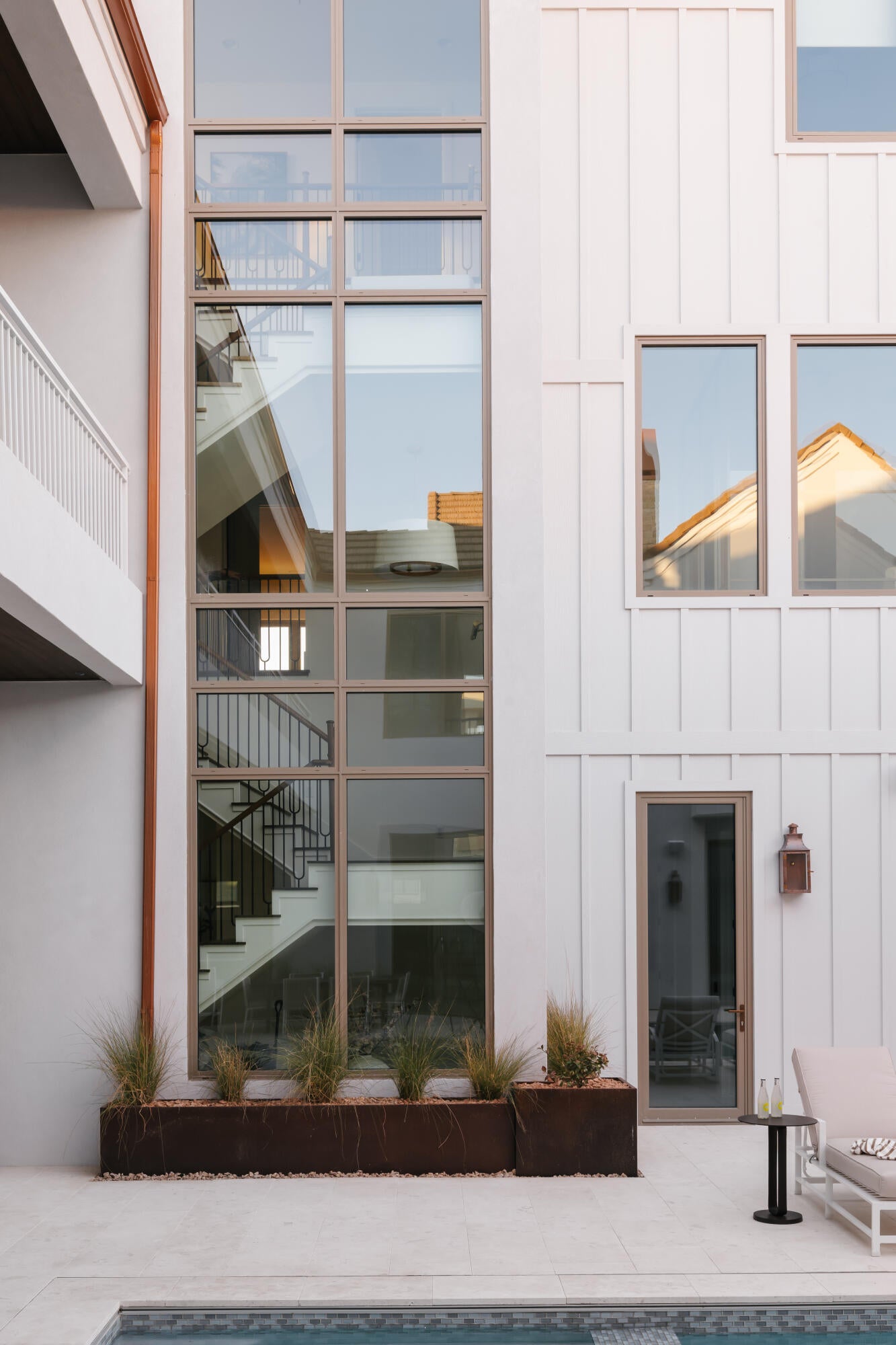 Exterior featuring a towering window wall, white board and batten siding, and a copper downspout