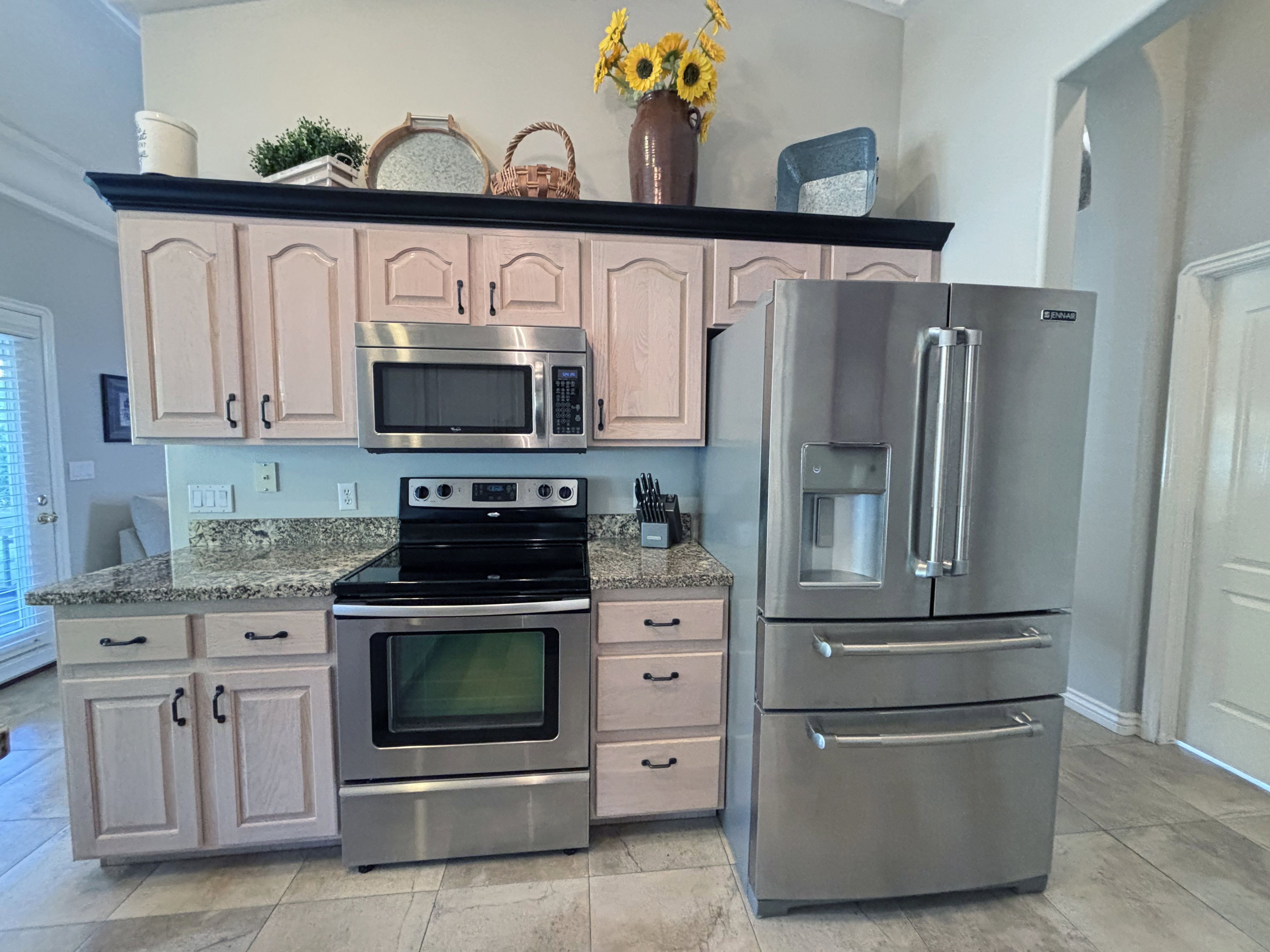 Kitchen featuring light wood-finish cabinetry with dark hardware, granite-style countertops, and a tile floor