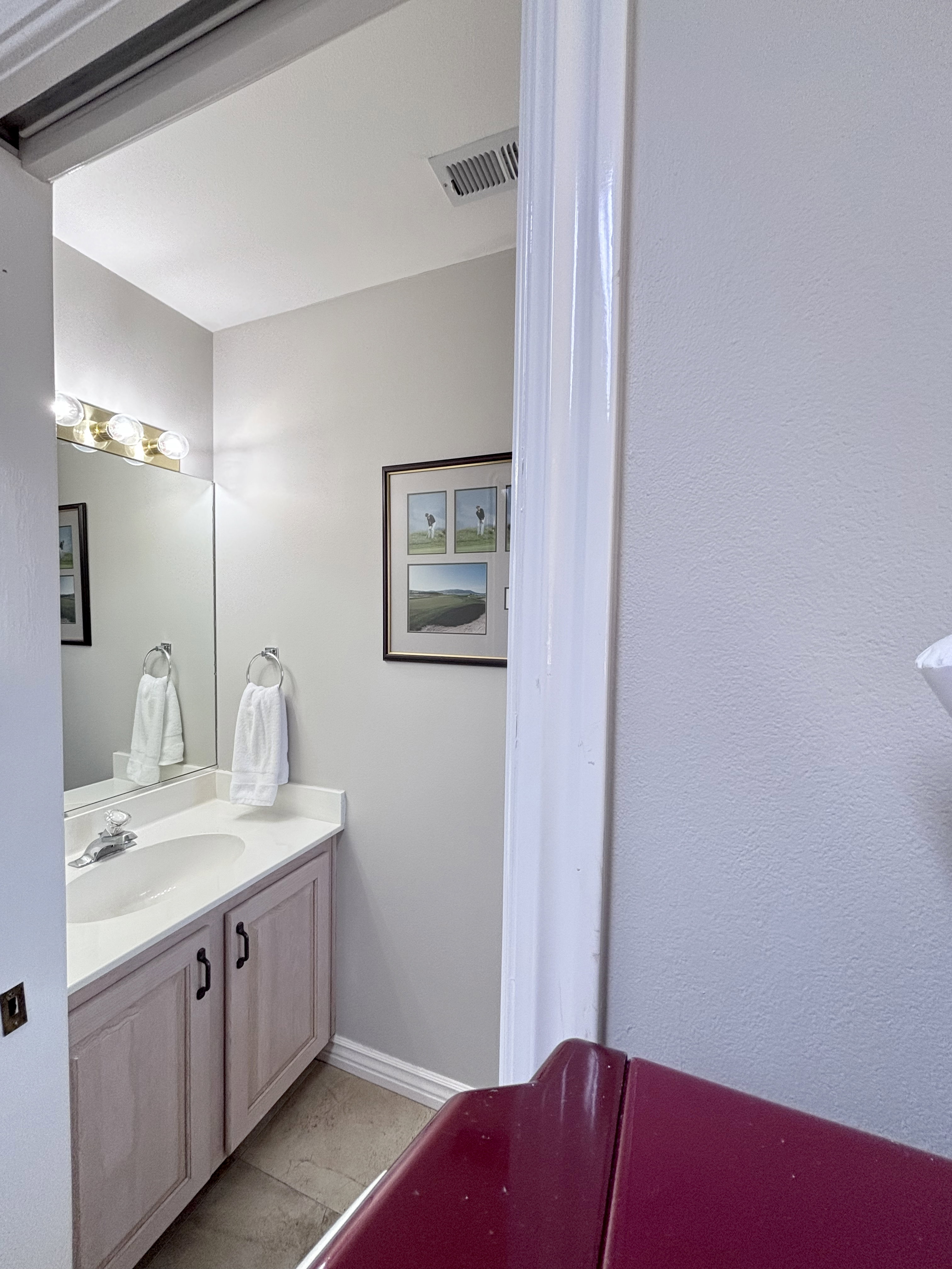 Vanity area featuring a light-toned wood-finish cabinet with dark hardware, a white countertop, and an integrated sink